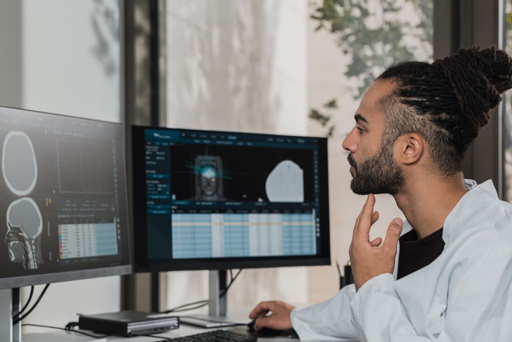 En man som jobbar inom vården tittar på två digitala skärmar som visar hälsodata i form av bilder, tabeller, grafer och andra visualiseringar. 