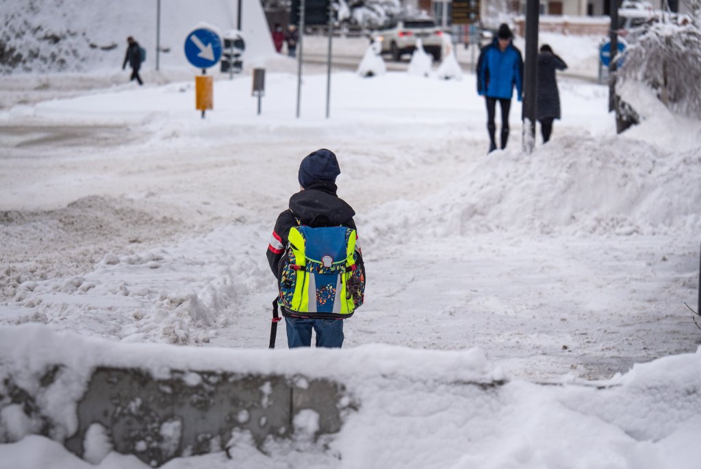Fotografi av ett barn som ska gå över gatan i en snötäckt stadsmiljö. Symboliserar en potentiellt farlig skolväg för barnet.