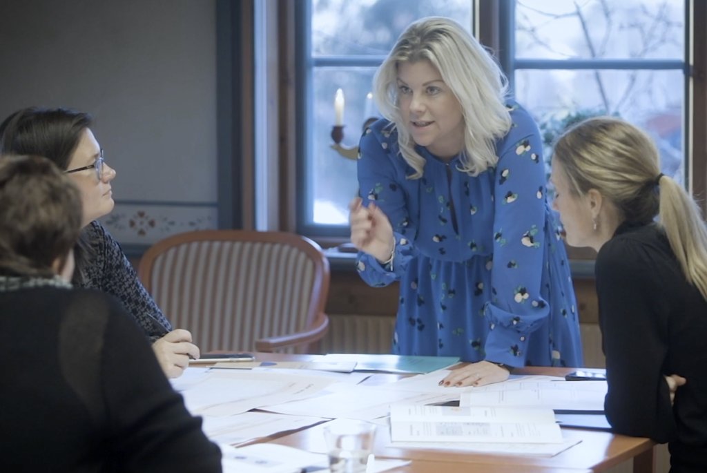 Tre personer arbetar vid ett bord fullt med papper på en utbildning som leds av Bouvets medarbetar Karin. 