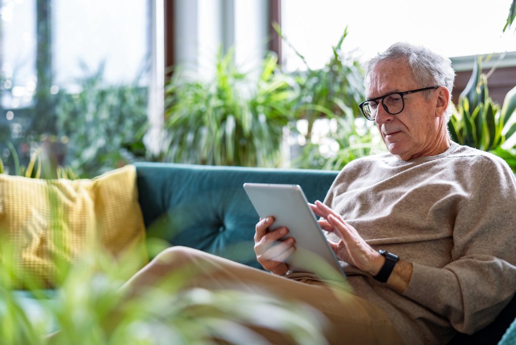 Senior man using digital tablet while sitting on sofa in living room at home