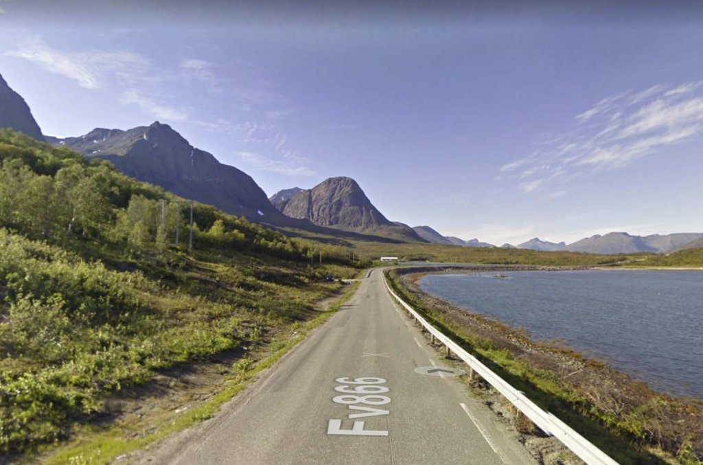 Fotografi med en asfalterad väg som går intill en norsk sjö eller fjord. Höga berg i grunden.