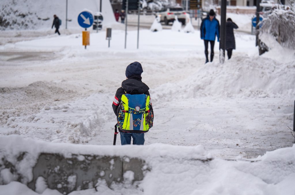 Fotografi av ett barn som ska gå över gatan i en snötäckt stadsmiljö. Symboliserar en potentiellt farlig skolväg för barnet.