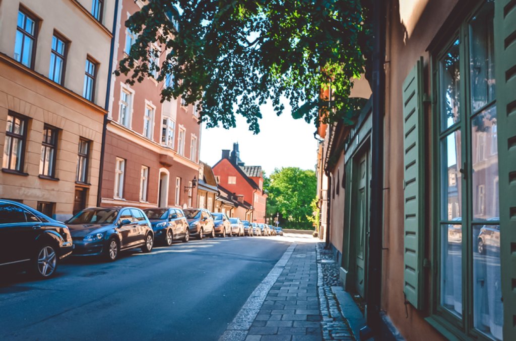 Fotografi som visar en gata i Stockholm med parkerade bilar framför färgglada hus.