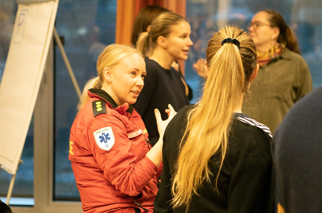 Fotografi från workshop i tjänstedesign med flera deltagare. En kvinna som jobbar inom ambulanssjukvården är i fokus och samtalar med en annan deltagare.